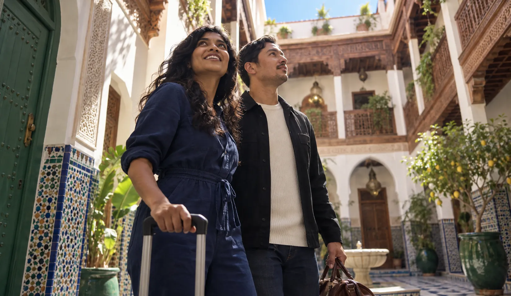 A smiling couple with luggage arriving in the sunlit courtyard of a boutique hotel