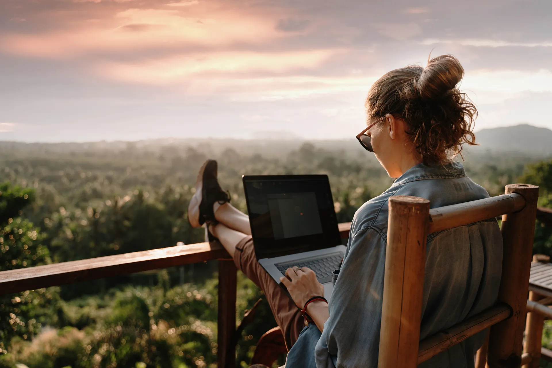 A host working on a laptop on a balcony at sunset