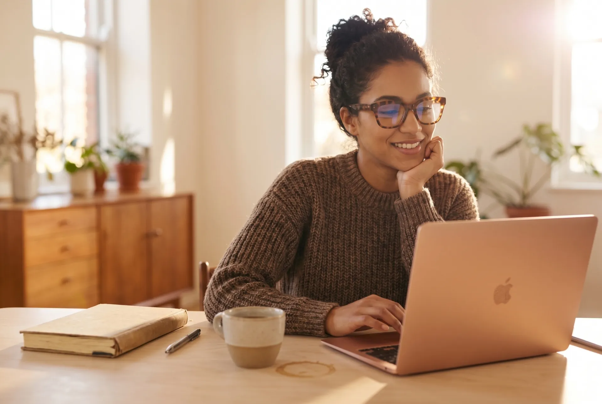 A host at a laptop by a sunny window with coffee